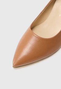 Brązowy skórzany płaski but z zaostrzonym noskiem, o gładkiej fakturze i delikatnym wycięciu po bokach. Podeszwa z subtelnym metalicznym akcentem.