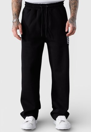 Schwarze Jogginghose mit elastischem Bund und Kordelzug. Verfügt über Seitentaschen und ein weißes Logo am linken Bein. Hergestellt aus weichem Stoff.