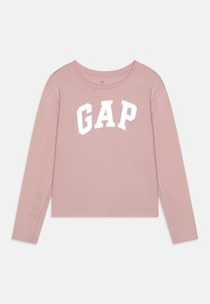 T-shirt à manches longues et coupe courte en coton rose doux avec un col rond et un graphique blanc "GAP" sur la poitrine. Texture lisse.