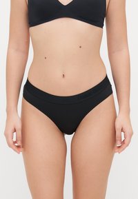 Zwarte katoenen bikini onderbroek met een gladde textuur en een medium taillehoogte. De tailleband heeft het logo "Organic Basics" in een contrasterende kleur.