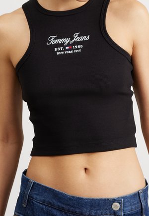 Kobieta w czarnym przyciętym topie z napisem "Tommy Jeans EST. 1985 New York City" oraz niebieskich dżinsach.