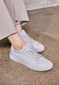 Baskets en cuir gris clair à texture lisse, avec un bout arrondi, un design à lacets et un logo discret sur le côté. Semelle blanche épaisse.