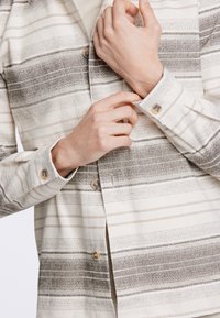 Camicia a righe button-up in tessuto beige e grigio, con colletto, polsini a bottoni e materiale testurizzato con linee orizzontali.