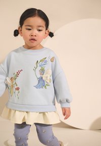 Jasnoniebieska bluza z haftem kwiatowej wróżki, zestawiona z białym falbaniastym dołem oraz liliowymi legginsami z drobnym kwiatowym wzorem.