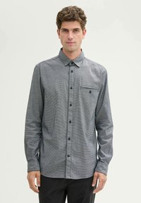 Grau langärmliges Hemd mit Knöpfen, strukturiertem Muster, Kragen und einer Brusttasche, kombiniert mit schwarzen Hosen.