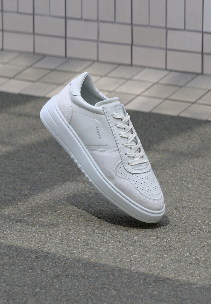 Zapatillas blancas que combinan cuero liso y ante, con detalles perforados, cordones planos y una suela acolchada.