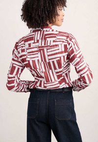 Camisa de rayas rojas y blancas con mangas largas y un tejido texturizado, combinada con pantalones de mezclilla azul oscuro que tienen bolsillos traseros.