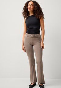 Top senza maniche nero e pantaloni a palazzo beige, entrambi realizzati in tessuto morbido e elastico. Le scarpe basse nere completano l'outfit.