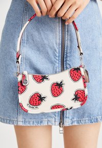 Witte leren handtas met rood aardbeienpatroon, zilveren beslag en een korte riem. Bovenaan met ritssluiting.