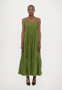 Abito maxi senza maniche in cotone verde oliva, caratterizzato da un collo a giro e una silhouette fluida. Abbinato a tacchi a punta neri.