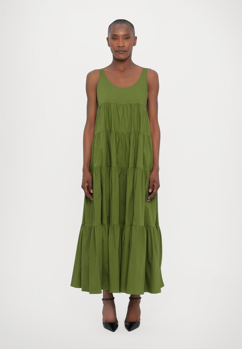 Abito maxi senza maniche in cotone verde oliva, caratterizzato da un collo a giro e una silhouette fluida. Abbinato a tacchi a punta neri.