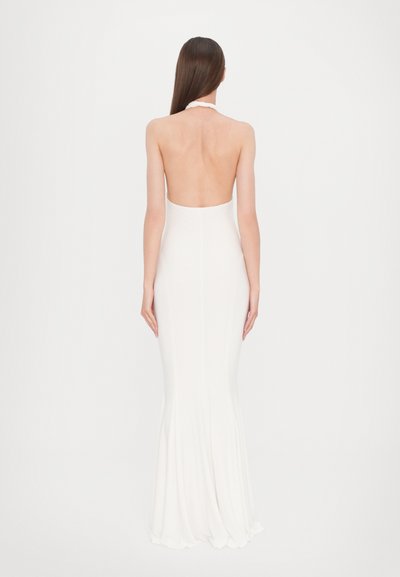 Vestido blanco, sin espalda, de largo hasta el suelo con una silueta ajustada, textura suave y dobladillo acampanado. Presenta un diseño de cuello halter.
