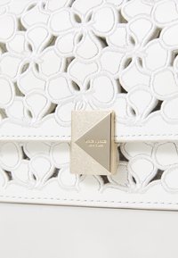 Borsa bianca in pelle con design traforato a fiori, ferrature color oro e chiusura triangolare con dettaglio del marchio in rilievo.