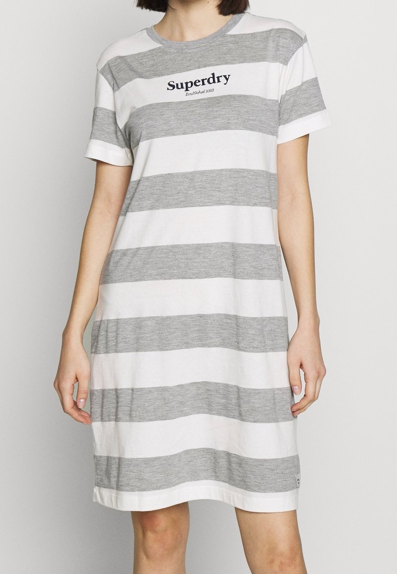 Femme portant une robe à manches courtes, longueur genou, avec de larges rayures horizontales grises et blanches et le logo "Superdry" sur la poitrine.