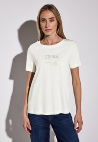 T-shirt blanc en coton à manches courtes, présentant un design graphique texturé beige avec le texte "ÈPURE SOLEIL" au centre.