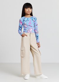 Haut à manches longues bleu avec des imprimés de dessins animés colorés et des cœurs, associé à un pantalon cargo beige avec des poches latérales, porté avec des baskets blanches.