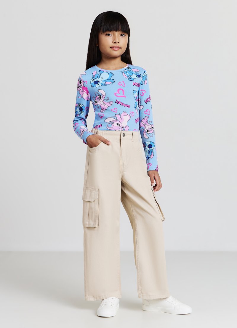 Haut à manches longues bleu avec des imprimés de dessins animés colorés et des cœurs, associé à un pantalon cargo beige avec des poches latérales, porté avec des baskets blanches.