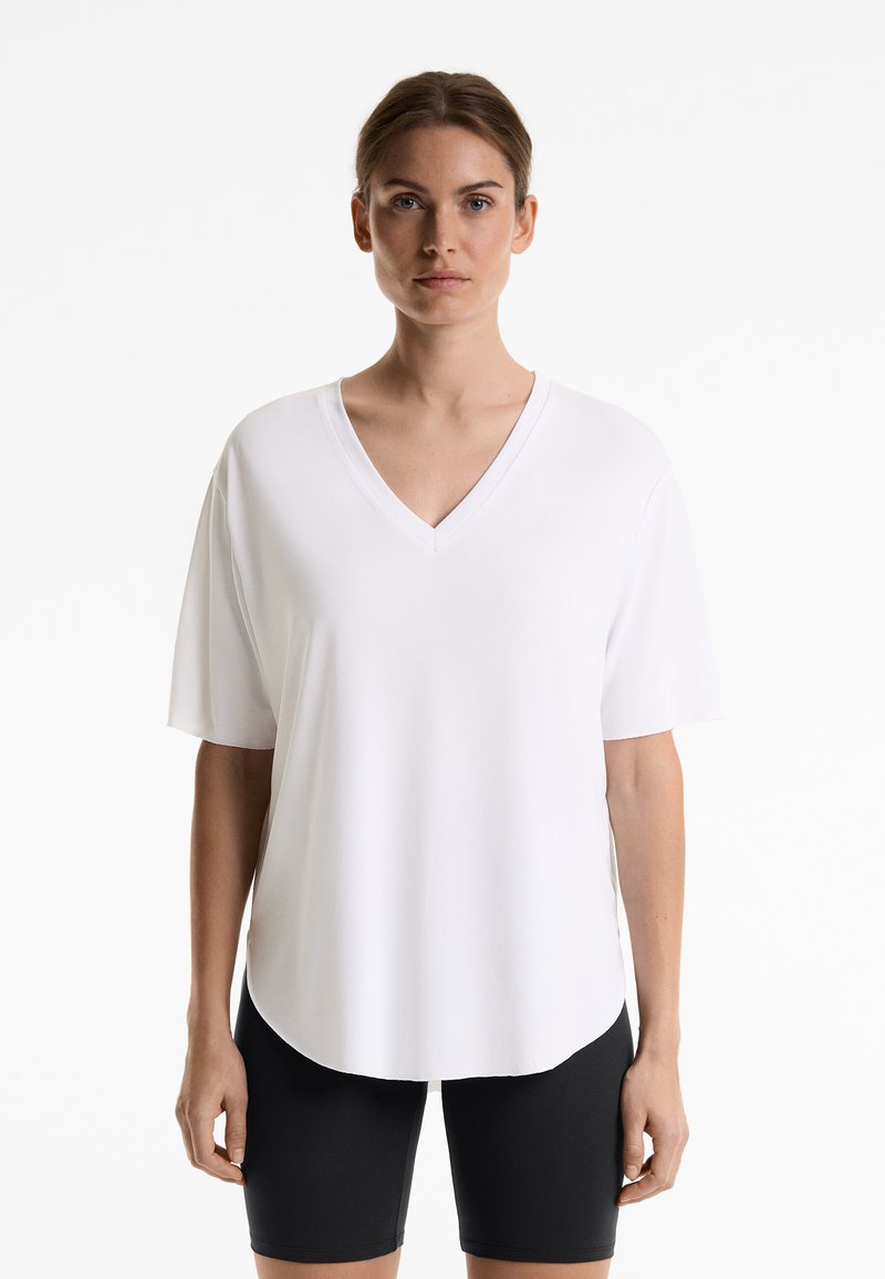 T-shirt blanc à col en V avec des manches courtes, fabriqué en tissu lisse. L'ourlet a une légère courbure, porté avec un short noir ajusté.