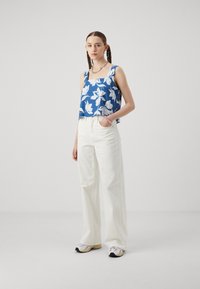 Blue floral crop top with white flowers, paired with high-waisted white wide-leg pants and multi-colored sneakers. Silver chain necklace.