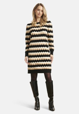 Knit dress with a chevron pattern in black, beige, and cream, featuring long sleeves and ribbed cuffs, paired with knee-high black boots.