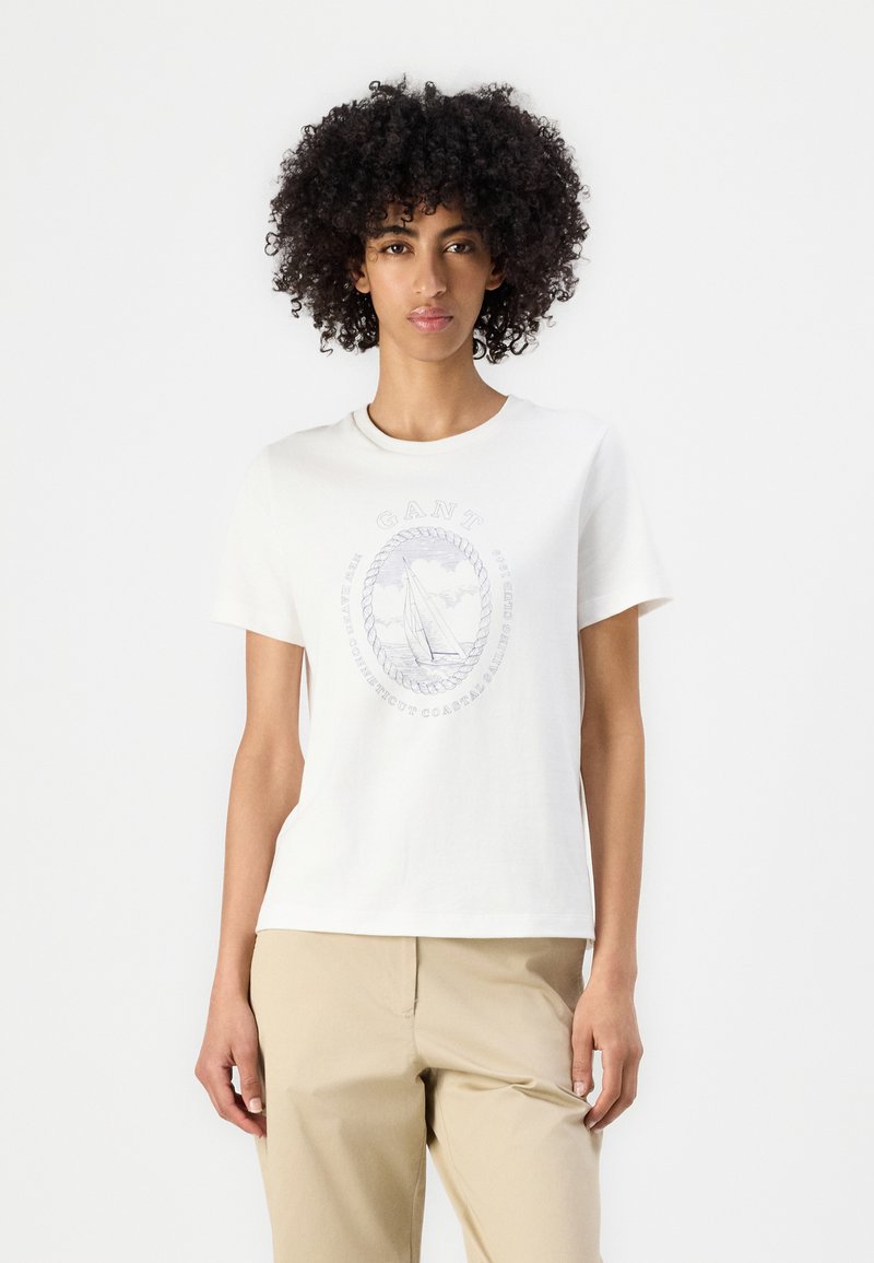 Hvid bomulds T-shirt med rund halsudskæring og korte ærmer. Har en båd grafik og tekst i lys blå tryk på forsiden.