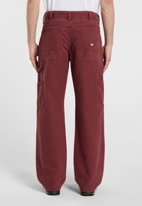Pantaloni cargo bordeaux realizzati in un tessuto resistente. Le caratteristiche includono gambe larghe, molteplici tasche e un logo sulla tasca posteriore.