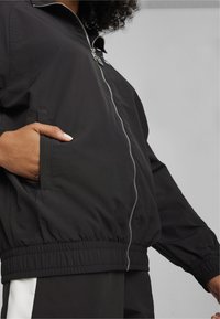 Sort letvægtsjakke med opretstående krave, lynlås foran, elastiske manchetter og sidelommer. Glat tekstur og løstsiddende design.