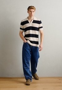 Tricou polo tricotat cu dungi orizontale negre și crem, mâneci scurte și guler. Asortat cu blugi largi din denim închis și pantofi maro.