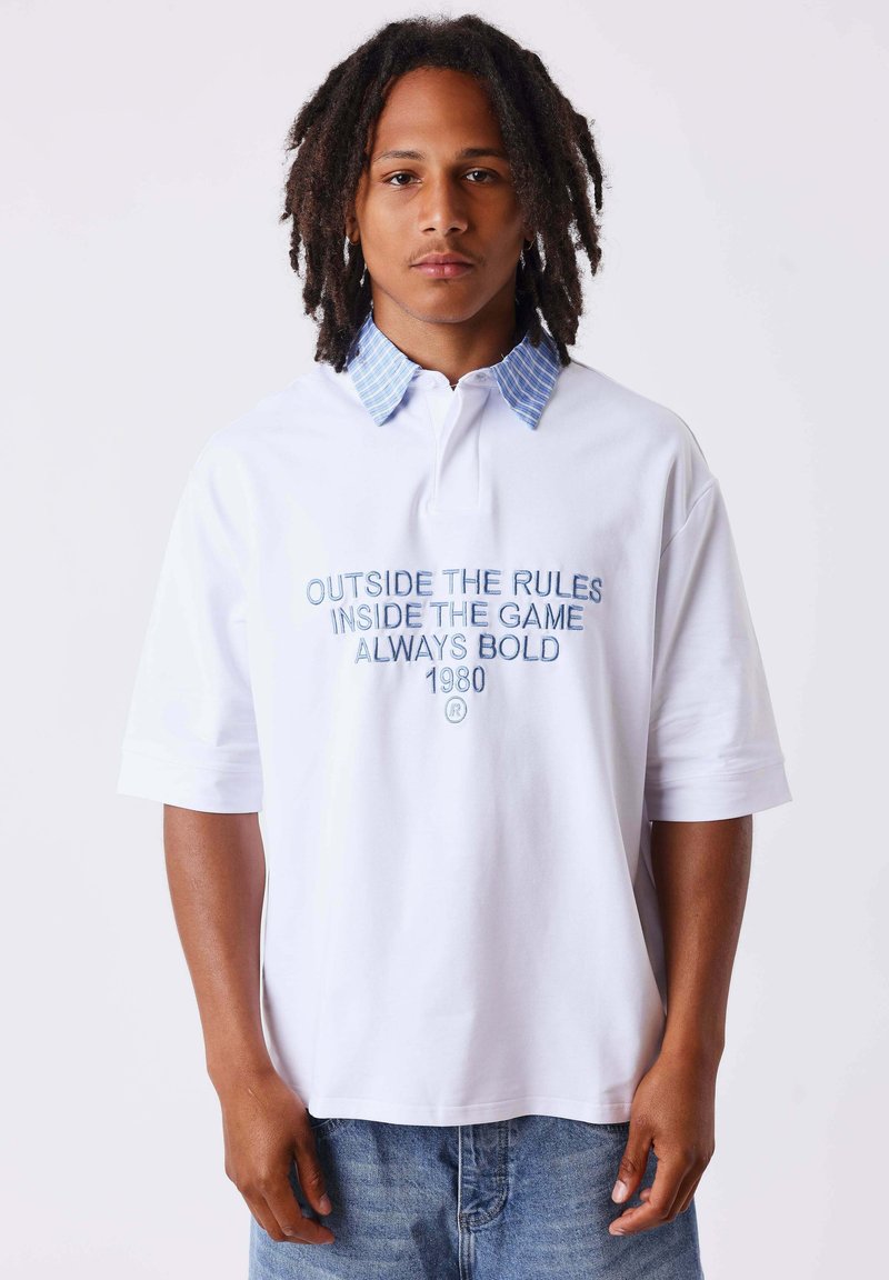 Jeune homme avec des dreadlocks portant un polo blanc avec un col rayé bleu et texte "Outside the rules inside the game always bold 1980."