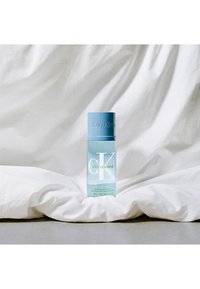 Le flacon de parfum Silky Coconut de Calvin Klein présente un design cylindrique transparent avec un capuchon bleu clair. Un texte est imprimé à l'avant.