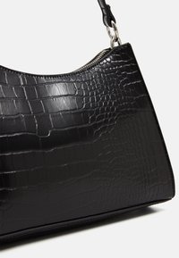 Mustasilmäkkilaukku, jossa on kiiltävä krokotiililaatta, hopeinen vetoketju ja irrotettava hihnan klipsi valkoista taustaa vasten.