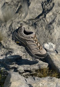 Bruine wandelschoen met een bovenwerk van mesh, contrasterende oranje veters en een gestructureerde rubberen loopzool. Bevat Vibram-merk op de zool.