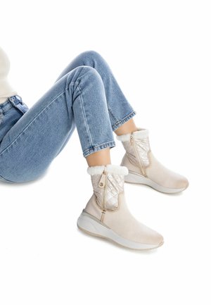 Botas de tobillo beige con parte superior acolchada y forro de piel sintética. Presentan un cierre de cremallera lateral y una suela ligera con un pequeño tacón.