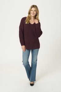 Bordeauxroter Strickpullover mit V-Ausschnitt, langen Ärmeln und lockerer Passform, kombiniert mit hellblauen Bootcut-Jeans und schwarzen Ballerinas. Texturierte Stoffdetails sind sichtbar.