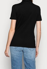 Svart polo-shirt i bomull med krage och korta ärmar. I kombination med ljusblå jeans som ger en avslappnad stil.