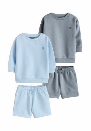 Divi zēnu sporta krekli ar īsām biksēm gaiši zilā un pelēkā krāsā, katram uz krūtīm ir neliels izšūts smaidīgs sejiņas attēls.