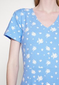 Vestido azul claro com mangas curtas e decote em V, apresentando pequenos padrões florais brancos por toda a peça e um corpete ajustado com uma saia rodada.