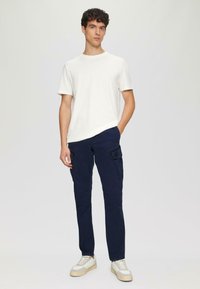 Biała koszulka bawełniana noszona z granatowymi spodniami cargo z bocznymi kieszeniami oraz kremowymi sneakersami z szarymi akcentami i beżowymi podeszwami.