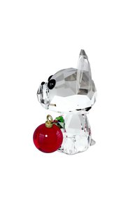 Przezroczysta kryształowa figurka psa trzymająca czerwoną ozdobę, z czarnymi akcentami na oczach, zielonymi detalami ostrokrzewu oraz gładką, fasetową teksturą.