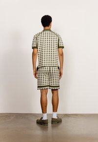 Rutigt stickat plagg i grön och krämfärgad, kortärmad topp med matchande shorts. Platt stickad textur, ribbade muddar och fållar, avslappnad passform.