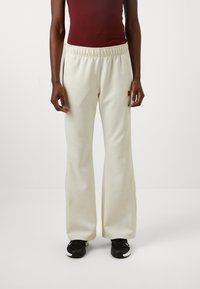 Pantalones anchos de color crema claro con cintura elástica y bolsillos laterales, combinados con zapatillas deportivas negras, que cuentan con un pequeño parche de logo.