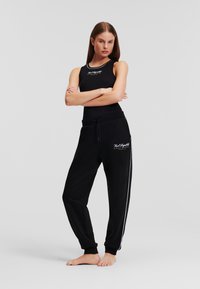 Black tank top and joggers featuring a white logo, made of soft fabric. Joggers have a drawstring waist and side stripes.
