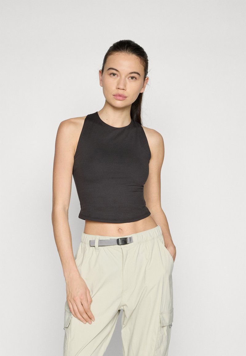 Zwarte mouwloze crop top met een hoge hals, gemaakt van gladde stof; gecombineerd met lichtbeige cargobroek met een riem.