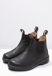 Botas de tobillo de cuero negro con paneles laterales elásticos, lengüetas de tiro y una suela de goma duradera; textura suave y diseño de punta redonda.
