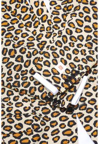 Leopard-Print-Anzug mit einem cremefarbenen Grund, kräftigen schwarzen und orangen Mustern, schwarzen Knöpfen und einem weißen Hemdärmels, der hervorblitzt.
