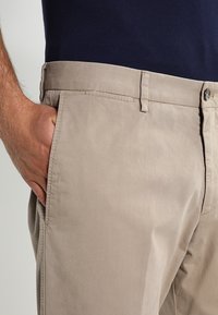 Beige katoenen chino's met een gladde textuur, platte voorkant met zakken en een enkele knoopsluiting. Gestyled met een marineblauwe top.