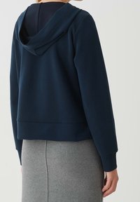 Felpa con cappuccio blu navy dal taglio morbido, in tessuto morbido e con polsini a coste, abbinata a una gonna grigia a vita alta.
