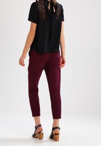 Blouse noire à manches courtes avec des détails en dentelle au dos, associée à un pantalon prune fuselé et des sandales à talons noires.