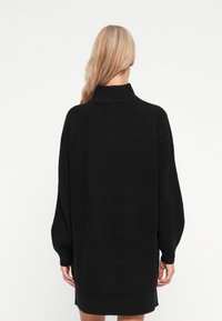 Melnā adītā kleita svārki ar augstu apkakli, garām raglāna piedurknēm, ribotiem aprocēm un apakšmalu. Mīksta tekstūra, brīvi pieguļošs stils, vidukļa garuma.