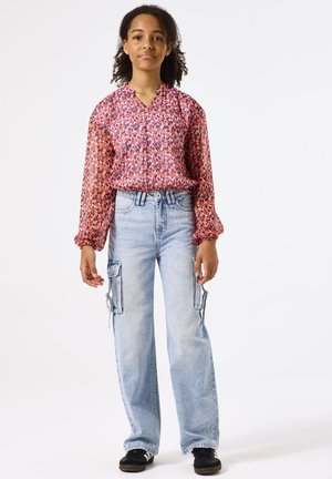 Blusa de patrón rojo y rosa con mangas largas y abullonadas y escote en V. Jeans de pierna ancha azul claro con bolsillos cargo. Zapatillas negras.